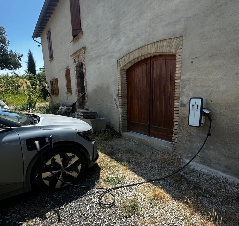 Borne de recharge murale en façade d’une maison, véhicule électrique en charge